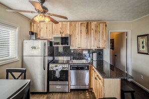 A compact kitchen with wooden cabinets, stainless steel appliances, and a ceiling fan.
