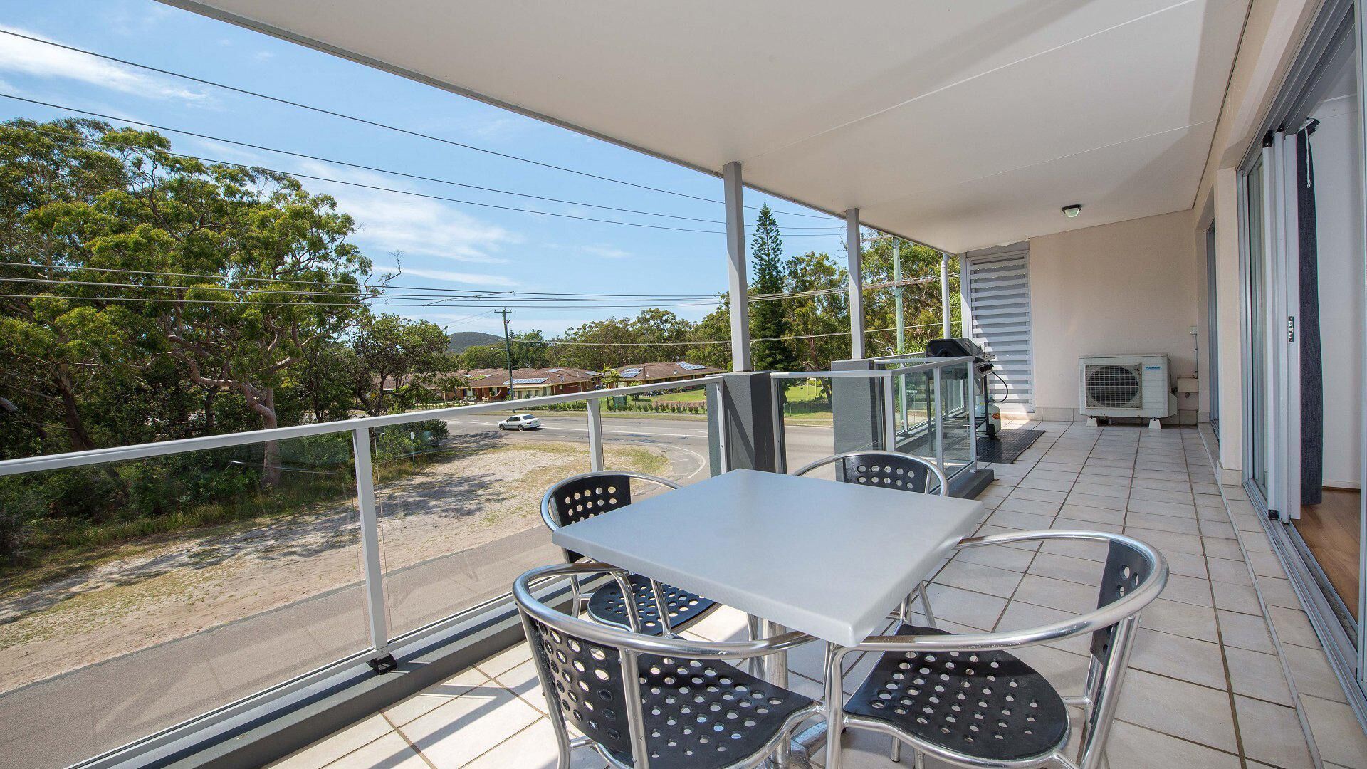 En balkon med bord og stole, der vender ud mod en vej og grønt område.