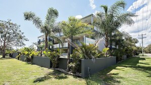 Un bâtiment moderne à deux étages, doté d’un balcon, et entouré d’une végétation luxuriante et de palmiers.