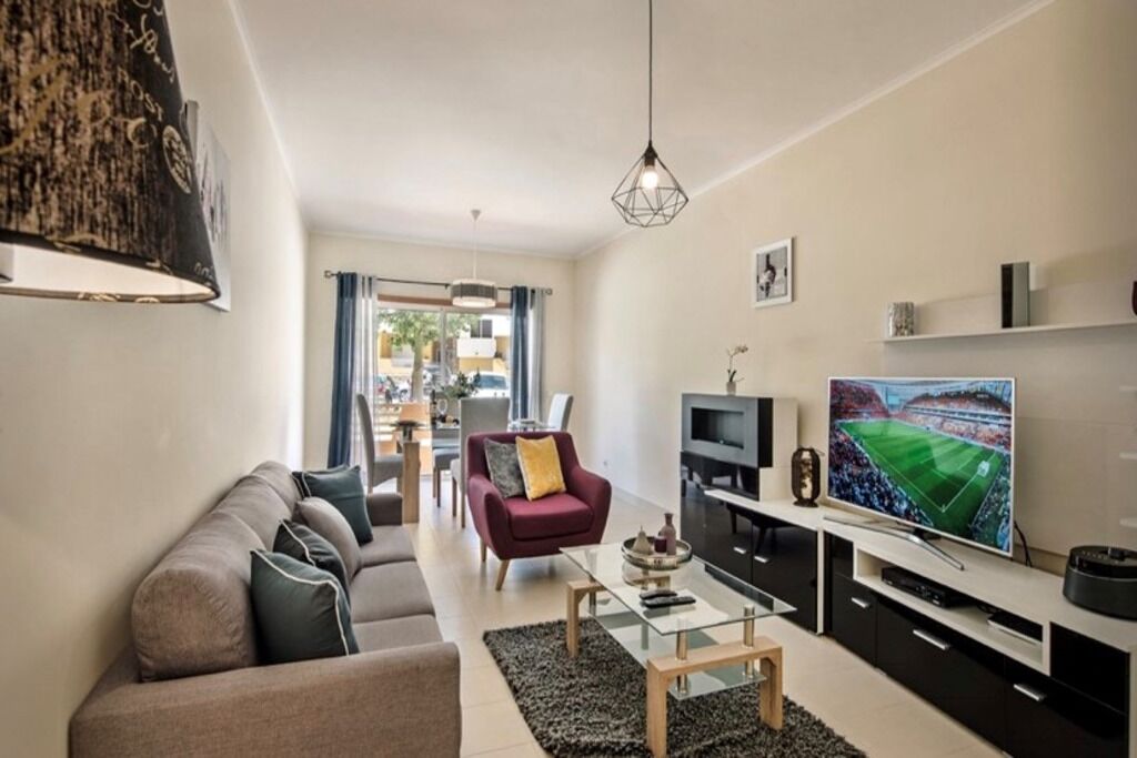 A modern living room with a sofa, coffee table, TV, and a dining area in the background.