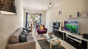 Una sala de estar moderna con un sofá, una mesa de centro, un televisor y un comedor al fondo.