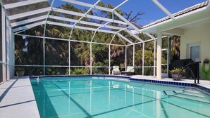 A swimming pool with a glass enclosure, surrounded by lounge chairs and potted plants. - Beautiful home on an 18 holes golf course (Sarasota)