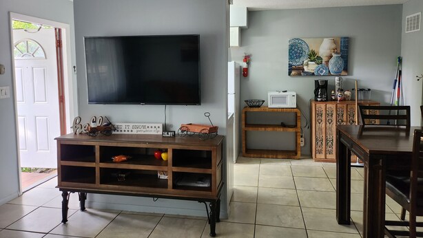 Een woonkamer met een flatscreen televisie, een houten tv-meubel, een eettafel en stoelen.