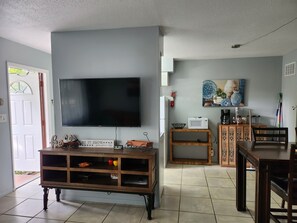 Una sala de estar con televisor de pantalla plana, mueble de madera para equipo audiovisual, mesa de comedor y sillas.