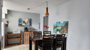 Een eethoek met een houten tafel en stoelen, een wit plafond en een schilderij van een rivierlandschap aan de muur.