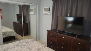 Een slaapkamer met een bed, een dressoir, een televisie en een airconditioning.