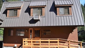 A two-story wooden cabin with a front porch, two windows with shutters, and a small door. - Hopes Cabin (Packwood)