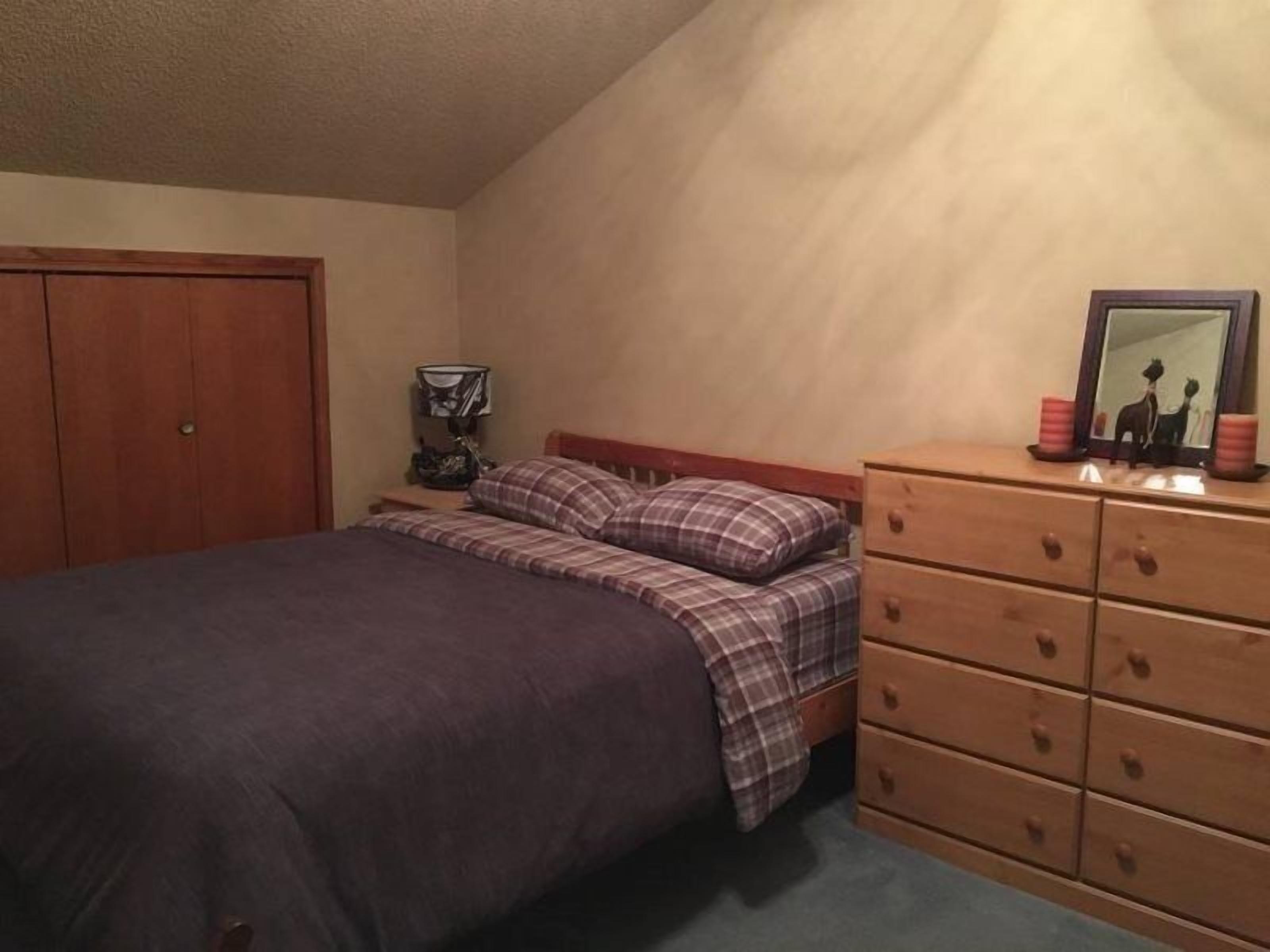 A bedroom with a bed, a nightstand, a dresser, and a mirror.