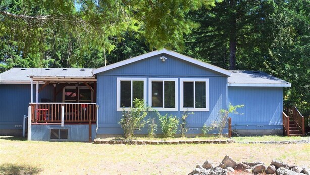 A single-story blue house with a porch, a small garden, and a stone wall in the foreground. - Rustic Rapids (Packwood)