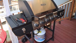 A portable grill with four burners, a side shelf, and a propane tank. - Rustic Rapids (Packwood)