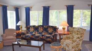 A living room with a floral sofa, a cushioned armchair, a glass coffee table, and two lamps on side tables. - Rustic Rapids (Packwood)