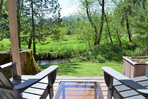 A deck with two Adirondack chairs facing a lush green landscape with a stream and trees. - Cabin on the Creek (Packwood)
