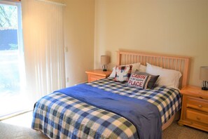 A bedroom with a bed, two bedside tables, a nightstand, a window with curtains, and a view of greenery outside. - Cabin on the Creek (Packwood)
