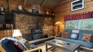 A cozy cabin interior with a stone fireplace, wooden walls, a sofa, and a coffee table.