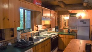A rustic cabin kitchen with wooden cabinets, a stove, a sink, and a refrigerator. - Cascade Log Cabin (Packwood)