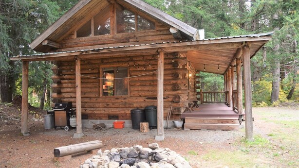 A rustic log cabin with a porch, a fire pit, and outdoor seating. - Cascade Log Cabin (Packwood)