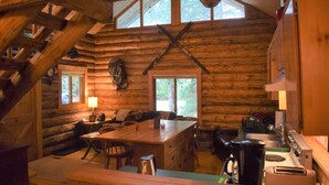 A rustic cabin interior with a wooden dining table, a sofa, and a kitchen area with a sink and stove. - Cascade Log Cabin (Packwood)