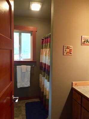 Een badkamer met een houten deur, een raam, een handdoek aan een rek, een gestreept douchegordijn en een klein fotolijstje aan de muur.