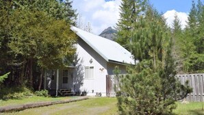 Une petite cabane blanche, dotée d’un toit en pente, entourée d’une forêt dense et d’une clôture en bois.