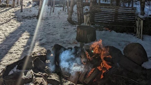Une forêt avec un feu de camp, un sol recouvert de neige et un banc en bois.