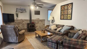 Un salon confortable avec une cheminée, un ensemble de canapés, un téléviseur et un ventilateur de plafond.