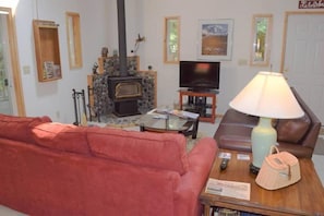 A cozy living room with a stone fireplace, a television, a red sofa, and a lamp on a wooden side table.