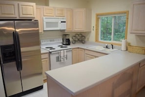 A modern kitchen with stainless steel appliances, a white countertop, and wooden cabinets.