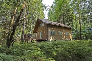 A wooden cabin with a deck, surrounded by dense forest.