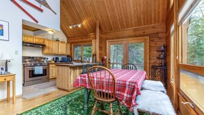 A cozy cabin interior with a wooden dining area, a kitchen with modern appliances, and large windows offering a view of the forest. - Trails End (Packwood)