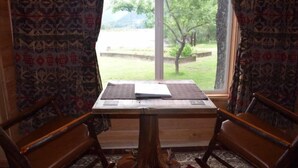 Une pièce avec une table en bois, deux chaises et une vue sur un jardin par la fenêtre.