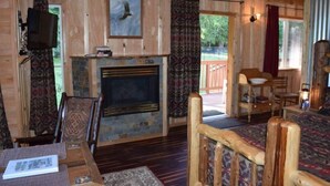 L’intérieur chaleureux d’un chalet avec une cheminée en pierre, des meubles en bois et une grande fenêtre donnant sur le paysage extérieur.