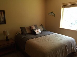 A bedroom with a bed, pillows, a nightstand, a lamp, a framed picture on the wall, and a window with a view. - Creekside Cabin (Packwood)