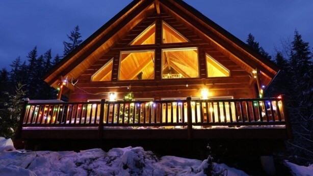 A wooden cabin with a balcony, large windows, and a deck with string lights. - Creekside Cabin (Packwood)