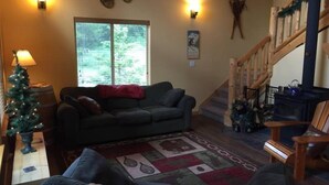A cozy living room with a dark green couch, a Christmas tree, and a fireplace. - Creekside Cabin (Packwood)