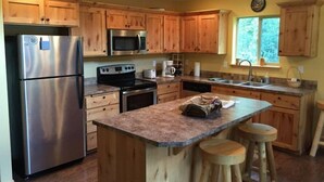 A kitchen with wooden cabinets, stainless steel appliances, a granite countertop, and a window with a view of trees. - Creekside Cabin (Packwood)