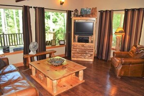 A living room with a wooden coffee table, leather sofa, and a TV mounted on a stone wall. - Antler Ridge (Packwood)