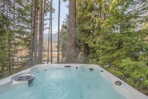 A hot tub surrounded by tall trees and a mountainous landscape. - Antler Ridge (Packwood)
