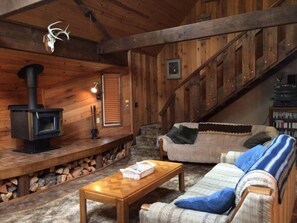 A rustic cabin interior with a wooden staircase, a sofa, a coffee table, and a fireplace.