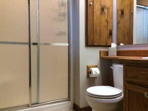 A bathroom with a shower, toilet, and wooden cabinet.