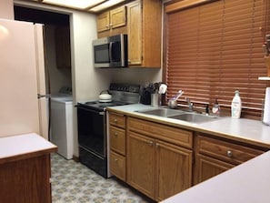 A compact kitchen with wooden cabinets, a microwave, a stove, and a sink.