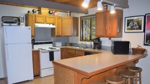 A kitchen with wooden cabinets, a white refrigerator, a stove, a sink, and a bar area with stools. - Rainier Retreat (Packwood)