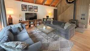 A cozy living room with a wooden ceiling, a large flat-screen TV, grey sofas, a coffee table, and a patterned rug. - Rainier Retreat (Packwood)