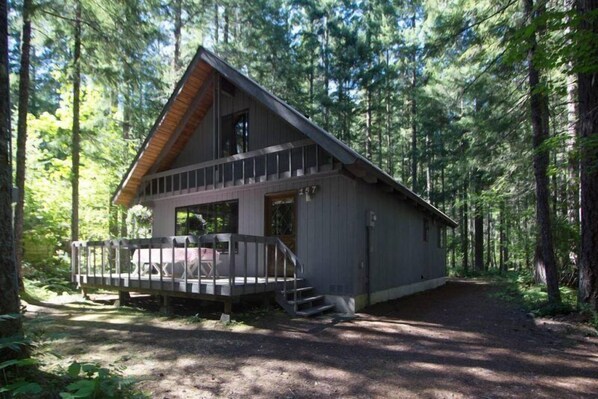 A cabin with a deck, surrounded by a forest.