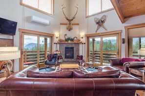 A spacious living room with leather sofas, a fireplace, and a mounted deer head. - Ravenwood (Packwood)
