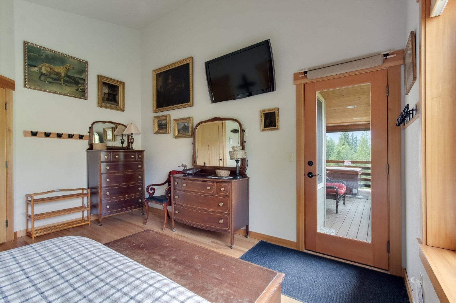 A bedroom with a bed, dresser, vanity, and a television. There is a door leading to an outdoor area.