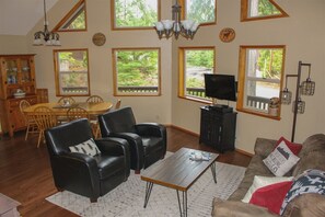 A spacious living room with a dining area, large windows, a television, and a cozy seating arrangement. - Cedar Grove Lodge (Packwood)