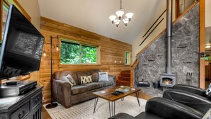 Ein gemütliches Wohnzimmer mit Kamin aus Stein, Holzwänden, einer Couch und einem Fernseher.