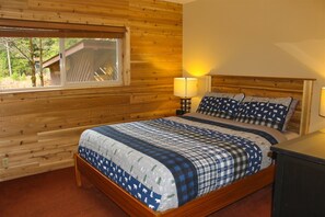 A wooden-paneled bedroom with a large bed, a window, and a nightstand with a lamp. - Cedar Grove Lodge (Packwood)