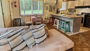 A cozy cabin interior with a dining area, kitchen, and a large window offering a view of the outdoors.