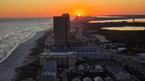 Een kuststadsgezicht in de zonsondergang, met een opvallend hotel met meerdere verdiepingen en een plat dak, gelegen nabij een strand en een weg.